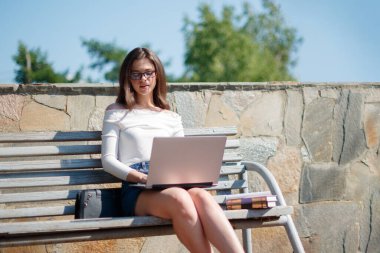 Kadın parkta bankta oturuyor ve dizüstü bilgisayar kullanıyor..