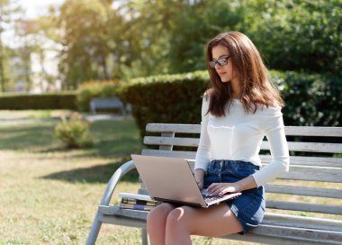 Kadın parkta bankta oturuyor ve dizüstü bilgisayar kullanıyor..