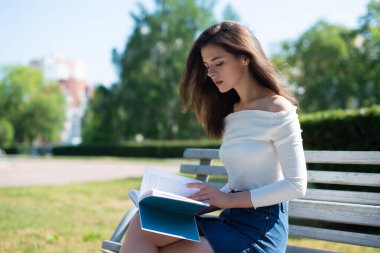 Genç bir kadın, bir yaz günü parkta bir bankta kitap okur.