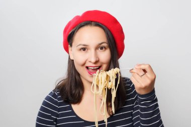 Kırmızı bereli genç bir kadın spagetti yiyor. Beyaz arkaplanda.