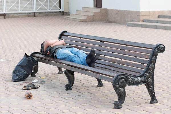 男はベンチで寝ている その横にはバッグや靴です ホームレスの概念 — ストック写真