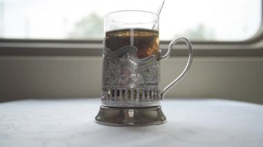 Rus demiryolu. Kompartımandaki masada geleneksel bir fincan tutacağında çay var. Bardaktan çay poşeti çıkaran bir elin yakın çekimi. Çay yap. Yolculuk.