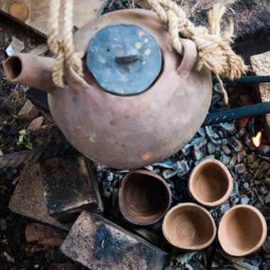 Dumanı tüten bir çaydanlık ve çay fincanı. Kil tencerede ateşte çay hazırlamak. Kamp gezisi, yolculuk..
