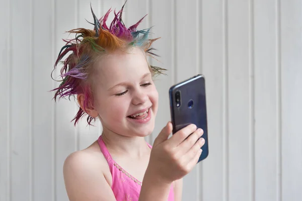 A girl in a smart dress and with a beautiful evening hairstyle communicates by phone, video. The child smiles at the person on the phone. Concept of an online party during the pandemic. — Stock Photo, Image