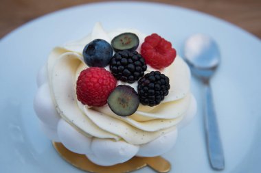 Krem şanti ve böğürtlenli bir turtanın yakın çekimi. Beyaz tabakta turta.