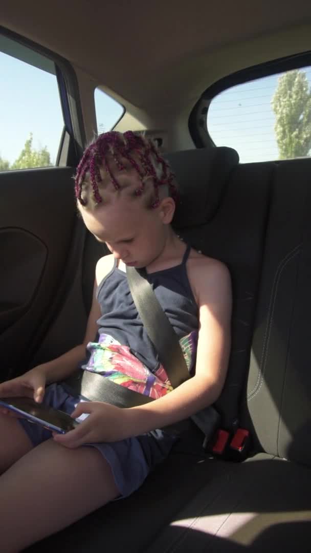 La chica está sentada en el coche, usando un cinturón de seguridad. El niño juega por teléfono. Adicción telefónica. Vídeo vertical. — Vídeo de stock