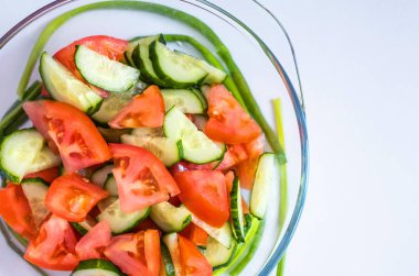 Taze sebze salatası, domates ve salatalık beyaz bir arka plan üzerinde duran bir şeffaf cam plaka.