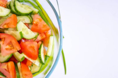 Taze sebze salatası, domates ve salatalık beyaz bir arka plan üzerinde duran bir şeffaf cam plaka.