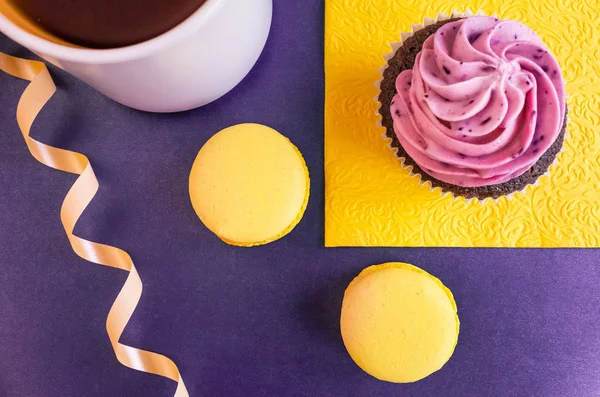 Purple cream cupcake on a yellow napkin and yellow macaroons on a blue background, geometric still life