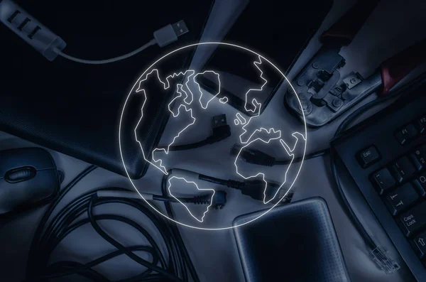 Items of information technology: cables, laptop, keyboard, smartphone, crimper. Contrasting light. In the foreground is a contour luminous image of the planet as a symbol of the globalization of information technologies