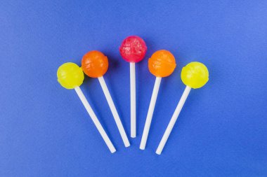 Kırmızı, turuncu ve sarı lolipoplar parlak mavi arkaplanda. Şeker konsepti, abur cubur. Kopyalama alanı.