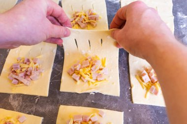 Bir adam jambon ve peynirli puf böreği pişiriyor. Puf puf, üzerine un serpiştirilmiş karanlık bir masanın üzerinde yatıyor. Çerçevede sadece erkek elleri var. Ev yapımı, yemek pişirme..