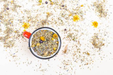 Hafif arka planda şifalı bitkiler üreten bir kupa. Etrafa saçılmış kuru çimenler ve çiçekler var. Sağlıklı çay kavramı, doğal soğuk algınlığı ilacı. Minimalizm.