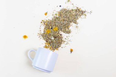 Beyaz bardak arka planda yatıyor. Etrafa saçılmış şifalı otlar ve çiçekler. Sağlıklı çay kavramı, doğal soğuk algınlığı ilacı. Minimalizm.
