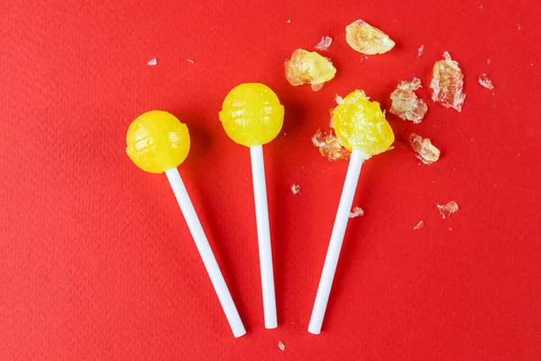 Three yellow lollipops on a bright red background. Some lollipop is chopped. The concept of sweets, junk food.