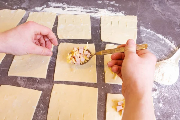 Male hands hold a spoon with ham and cheese on a rolled puff pastry. Filling for puff pastries. The concept of home baking, cooking.