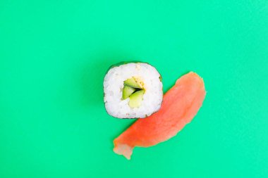 Parlak yeşil arka planda salatalık, susam tohumu ve zencefille yuvarlan. Japon yemeklerinin minimalist konsepti. Düz yerde, üst tarafta. Boşluğu kopyala.