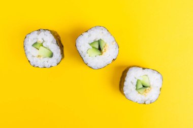 Parlak sarı arka planda salatalık ve susam tohumlu rulo. Japon yemeklerinin minimalist konsepti. Düz yerde, üst tarafta. Boşluğu kopyala.