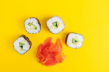 Parlak sarı arka planda salatalık, susam tohumu ve zencefilli rulo. Japon yemeklerinin minimalist konsepti. Düz yerde, üst tarafta. Boşluğu kopyala.