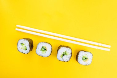 Salatalık ve susam tohumlu rulo ve parlak sarı bir zemin üzerinde çubuklar. Japon yemeklerinin minimalist konsepti. Düz yerde, üst tarafta. Boşluğu kopyala.