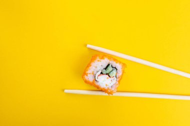 Parlak sarı arka planda tobiko havyarı, salatalık ve yengeç etiyle yuvarlan. Minimalist stil Japon yemeği konsepti. Düz yatıyordu. Üst Manzara. Boşluğu kopyala.