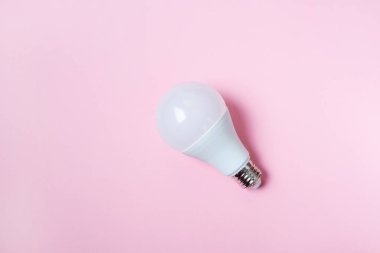 Öncü ampul, pastel pembe bir arka planda yatar. Enerji tasarrufu kavramı. Minimalizm, üst görünüm, düz uzanma, metin için yer.