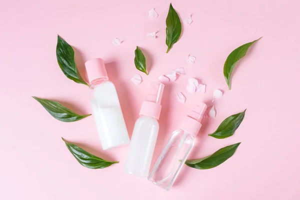 Transparent bottles with organic cosmetics on a pastel pink background. Concept of eco friendly cosmetic, cruelty free. Around the bottles are flower petals and green leaves. Minimalism, place for text.