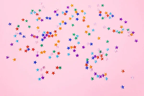 Multi-colored rhinestones in the form of stars on a pastel pink background. The concept of a holiday, party, birthday. Minimalism. Copy space.