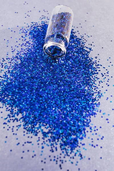 Close-up of blue sparkles in a transparent small bottle. Beautiful deep color and overflow. The concept of a holiday, party. Place for text.