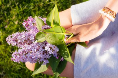 Diz çökmüş bir kadının elinde mis kokulu leylak çiçekleri. Romantik bir bakış. Parlak bahar tatili konsepti.