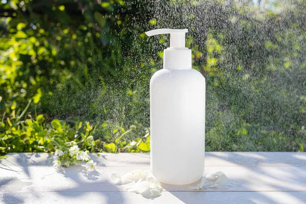 White cosmetic bottle with dispenser on a background of greenery. Spectacular splashes of water in the air. The concept of freshness, beauty, natural organic cosmetics, skin care.