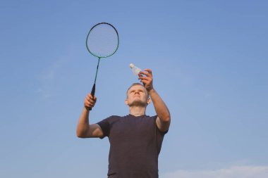 Genç beyaz adam mavi gökyüzünün arka planında badminton oynuyor. Amatör badminton oyunu konsepti, açık hava aktiviteleri. Kopyalama alanı, alt görünüm.