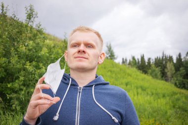 Karantina sona eriyor, yalnız yürüyor. Avrupalı genç sarışın erkek, çimen ve ağaçlarla kaplı bir tepenin arkasındaki parkta tek kullanımlık tıbbi maskeyi çıkarıyor..
