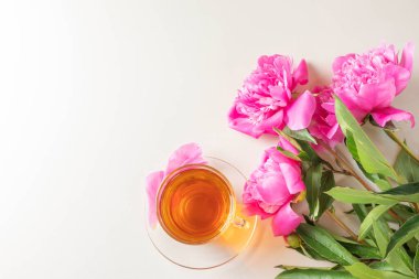 Pembe parlak şakayıklar ve şeffaf fincanda bir fincan çay ve arka planda bir fincan çay. Kopyalama alanı, üst görünüm. Şirin, hoş, zarif bir kadın yatağı..