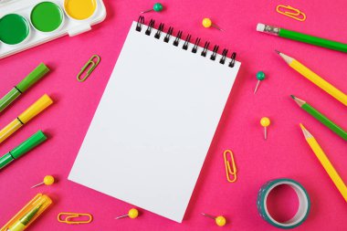 Okula dönüş kavramı. Boş sayfası olan bir spiral üzerinde not defteri. Okul kırtasiyesi düz: kalemler, kalemler, keskinleştirici, makas, cetvel, parlak pembe kağıt arka planda ataçlar. Kopyalama alanı.