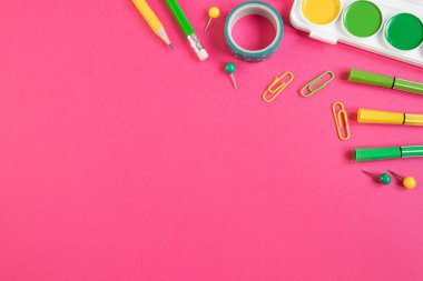 Okula dönüş kavramı. Okul kırtasiyesi düz: kalemler, kalemler, açıcı, cetvel, parlak pembe kağıt arka planda ataçlar. Kopyalama alanı.