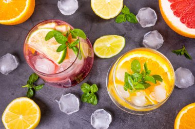 Koyu arkaplanda şeffaf gözlüklü soğuk bir kokteyl. Bir dilim portakal, limon, greyfurt, buz ve nane. Üst manzara, düz yatak, minimalizm Yaz mevsimi narenciye, alkolsüz içecek, kokteyl