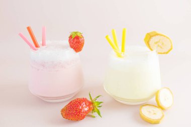 Çilekli ve muzlu milkshake şeffaf bardakta hafif bir arka planda. Yakınlarda çilek ve muz var. Lezzetli taze içecekler, kahvaltıda sağlıklı yiyecekler ve atıştırmalıklar..