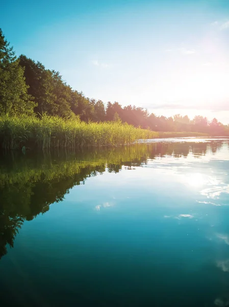 Summer landscape: the sky with clouds and the forest on the horizon are reflected in the clear water of the lake. Copspace. The concept of a relaxing holiday, the beauty of nature.