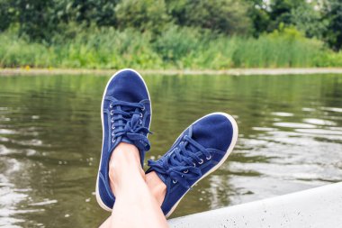 Suyun arka planına karşı mavi spor ayakkabılı bir tekne. Yaz tatili konsepti, rahatlama..