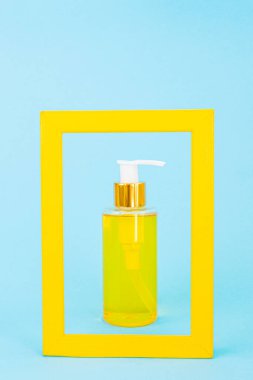 Doğal yağlı bir şeker kutusuyla birlikte kozmetik şişesi sarı çerçeveyle çerçevelenir. Mavi arka plan. Organik esansların, güzelliğin ve sağlık ürünlerinin şık bir konsepti. Minimalizm, boşluğu kopyala.