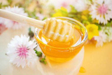 Bal için bir kaşık, bal yakın plan, aşağıda - bir damla. Arka planda kır çiçekleri var. Çiçek kavramı tatlım, organik, sağlıklı yiyecekler.