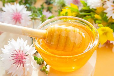 Bal için bir kaşık, bal yakın plan, aşağıda - bir damla. Arka planda kır çiçekleri var. Çiçek kavramı tatlım, organik, sağlıklı yiyecekler.