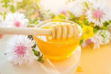 Bal için bir kaşık, bal yakın plan, aşağıda - bir damla. Arka planda kır çiçekleri var. Çiçek kavramı tatlım, organik, sağlıklı yiyecekler.