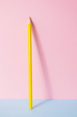 Okula dönelim. Pembe-mavi arka planda sarı bir kalem duruyor. Çocukların yaratıcılığının yaratıcı minimalist konsepti, çizim.