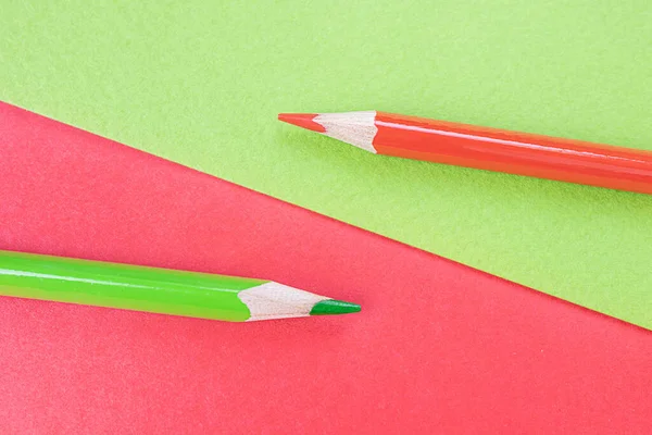 Back to school. Red and green pencils lie on the background of the same colors. Creative minimalistic concept of children\'s creativity, drawing.