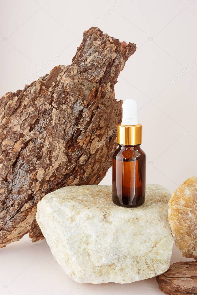 A bottle of natural essential oil on a stone, next to a tree bark with a beautiful texture. Concept for natural essences, organic cosmetics, aromatherapy, spa.
