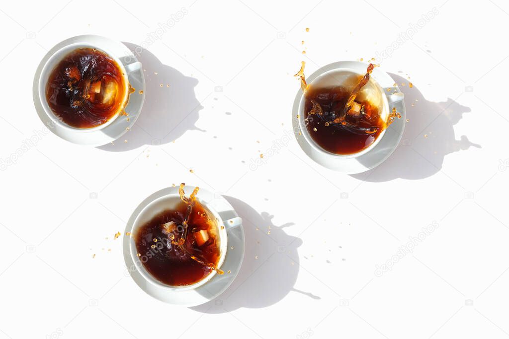 Black coffee in white cups, top view. Sugar lumps are thrown into the cup, spectacular splashes are spilling out of the cup. White background.