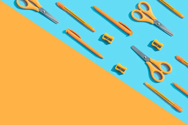 Back to school. Office - orange scissors, pens, sharpener on a blue background. Top view, flat lay.