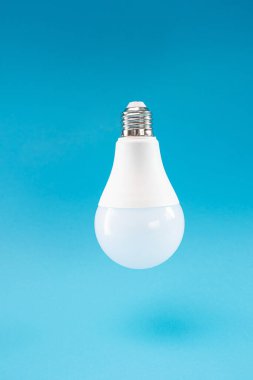 Mavi arka planda beyaz bir LED lamba havada asılı duruyor gibi görünüyor, havalanmanın etkisi. Mavi arkaplan, kopyalama alanı, minimalizm.